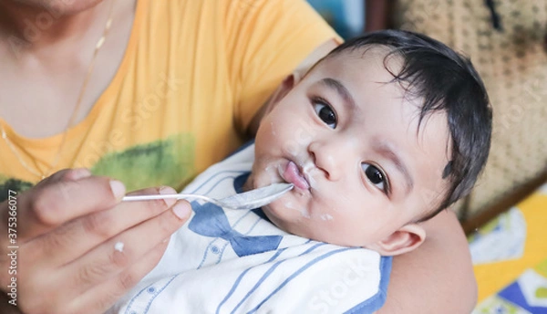 Fototapeta an infant toddler baby boy after weaning eating solid food with spoon