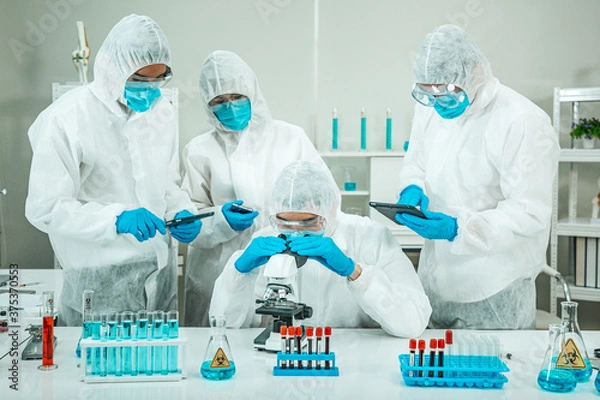 Fototapeta Group of Scientists wear Face Mask working in Lab while Checking Blood Sample by micro scope On Background.