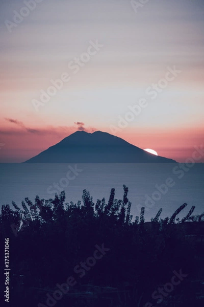 Fototapeta Amazing view of the Stromboli Volcano at sunset, wit the sun going down and amazing sea and sky colors. View form the coast of Calabria, Italy, in the touristic destination of Tropea.