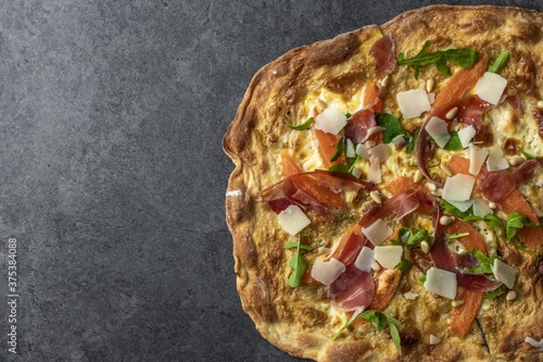 Fototapeta Pizza with jamon serrano prosciutto, melon, arugula salad and pine nuts. Flammkuchen, Tarte Flambee. Top view. Copy space