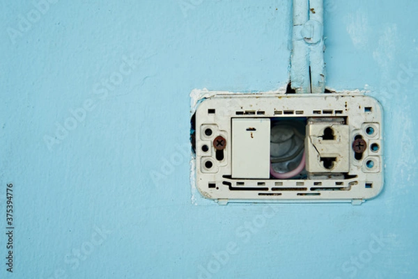 Fototapeta Power switch and defective plug, dirty and dangerous, No maintenance electric plug, on blue pastel wall.