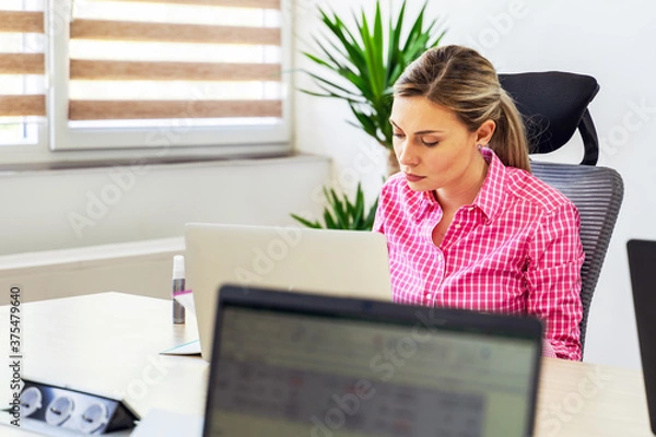 Fototapeta Young caucasian woman entrepreneur or manager sitting at the office at company having a meeting - Female CEO working on business day in front of laptop computer reading or writing notes