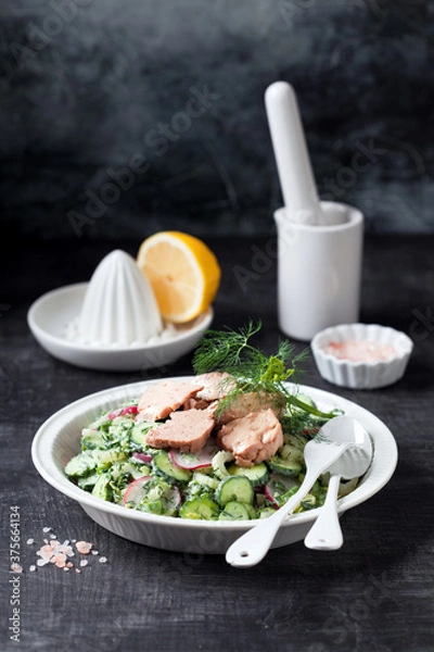 Obraz Fresh vegetables salad (radishes, cucumbers, avocado, celery, dill, green onions) with yogurt dressing and canned cod liver, selective focus