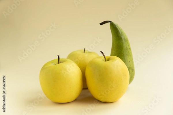 Fototapeta yellow golden delicious apples and a pear on a yellow background