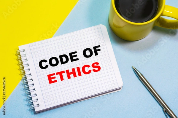 Obraz CODE OF ETHICS on a notepad on a blue-yellow background, a cup of coffee and a pen. Business concept