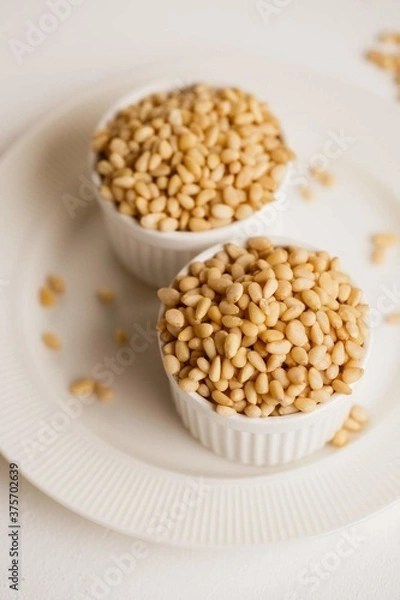 Obraz two cups with peeled pine nuts on a white background