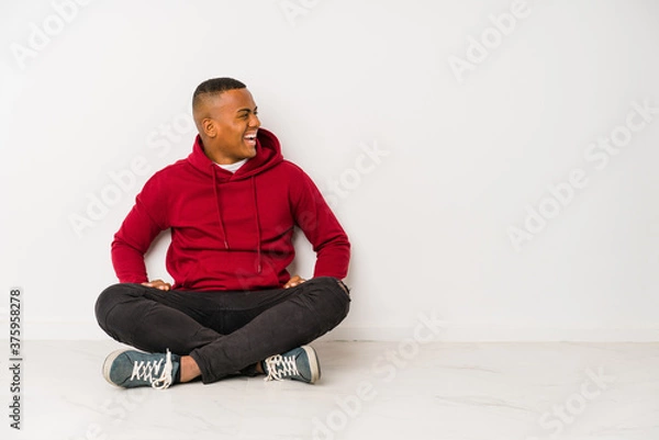 Fototapeta Young latin man sitting on the floor isolated shouting towards a copy space