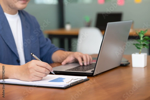Obraz Asian business man use labtop and note job on paper in office.