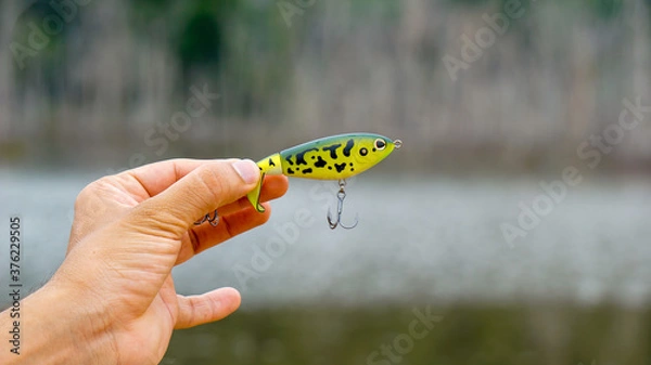 Fototapeta fishing lure held in hand,a fishing lure is a type of artificial fishing bait used to attract fish. Lures come in many different shapes, sizes, and colors, each designed to attract fish