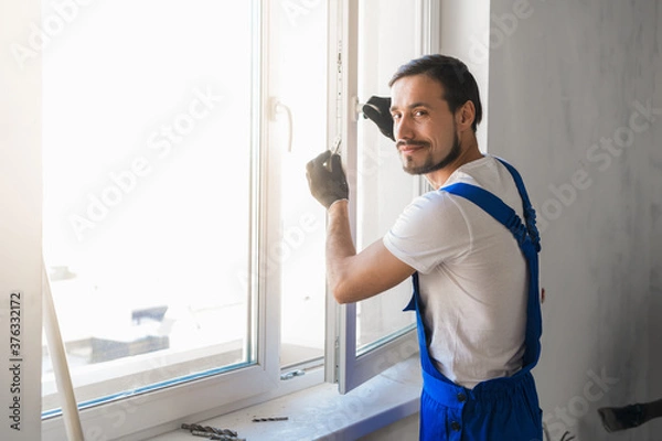 Fototapeta Male worker in overalls installs a window and poses at the camera