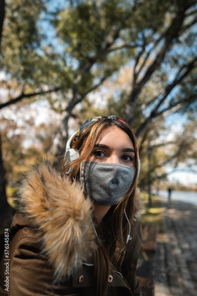 Fototapeta A woman wearing face mask sitting at park and looking at camera during covid 19 pandemic. Vertical