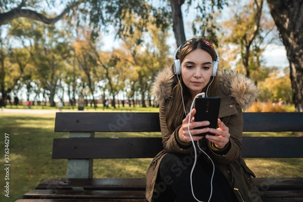 Fototapeta A beautiful caucasian woman sitting on a bench and using her smartphone. Copy space