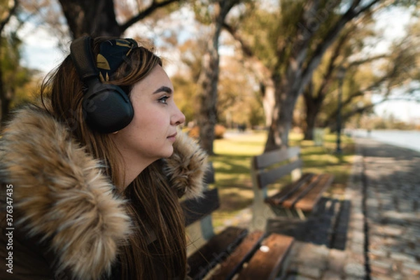 Fototapeta A pretty caucasian woman listening music at park and looking at side. Copy space