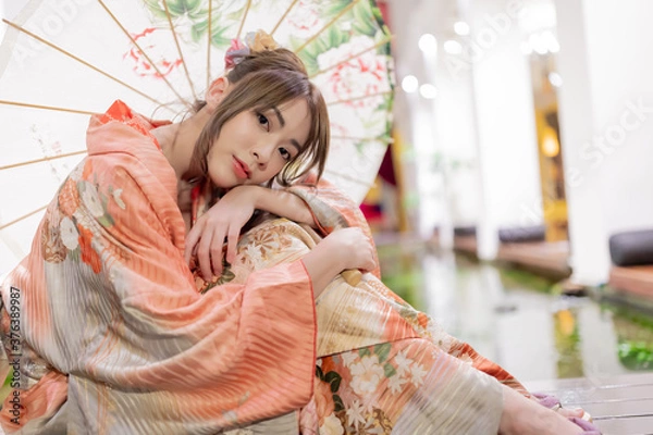 Obraz Young woman in traditional Japanese kimono with an umbrella  and looking at camera, Japanese concept of kimono and yukata.