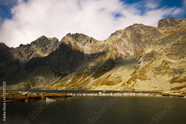 Fototapeta A mountain lake under the moutnains on a cloudy autumn day