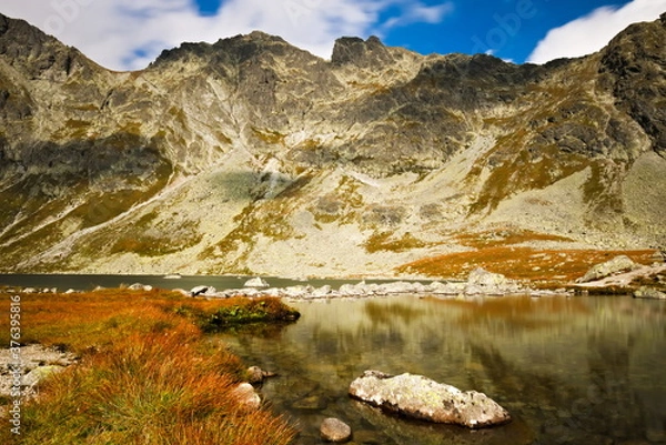 Fototapeta Mountain lake under the mountaintops  with a rock in the foreground