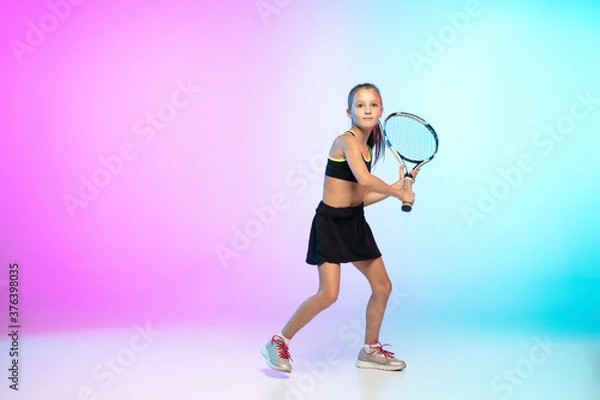 Fototapeta Running high. Little tennis girl in black sportwear isolated on gradient background in neon light. Little caucasian model, sport kid training in motion and action. Sport, movement, childhood concept.