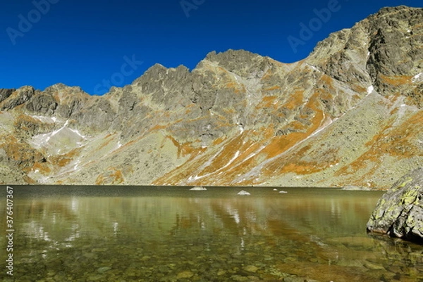 Fototapeta A lake under mountain peaks with clear sky in autumn
