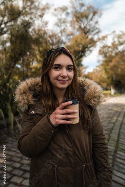 Fototapeta A caucasian woman smiling at camera while holding a coffee at park