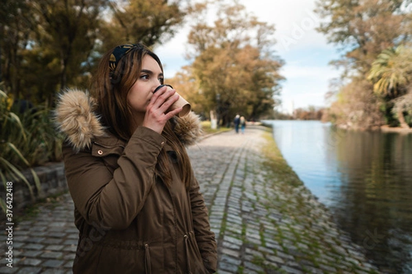 Fototapeta A pretty caucasian woman drinking a coffee while enjoying a walk at park. Copy space