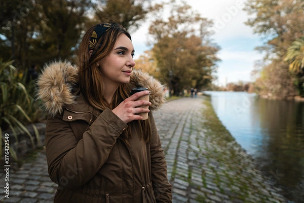 Fototapeta A pretty caucasian woman smiling while holding a coffee and enjoying a walk at park. Copy space