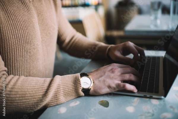Fototapeta Crop man typing on laptop keyboard
