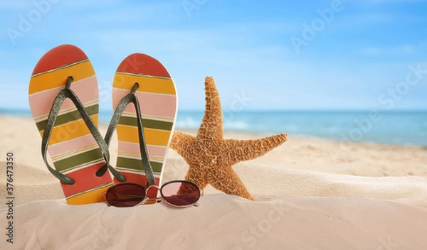Fototapeta Klapki i stylowe okulary przeciwsłoneczne na piasku w pobliżu oceanu, miejsce na tekst. Akcesoria plażowe