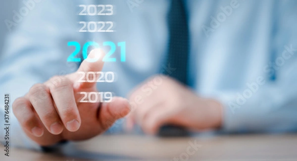 Fototapeta Nowy rok 2020 zmienia się na koncepcję 2021, dotykając ręką wirtualnego ekranu 2021.
