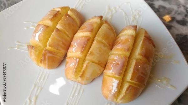 Fototapeta Buttered bread topped with sweetened condensed milk on a white plate.