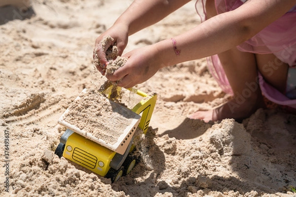 Fototapeta Child playing in a sandbox with a toy