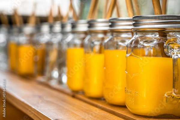 Fototapeta Orange juice in mason jars lined up on a wooden table outside
