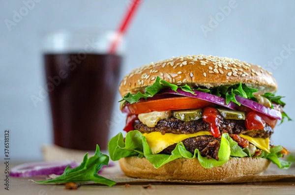 Obraz juicy powerful burger with beef and vegetables on a bun with sesame seeds.