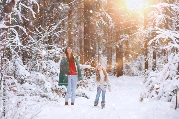 Fototapeta Young family for a walk. Mom and daughter are walking in a winter park.