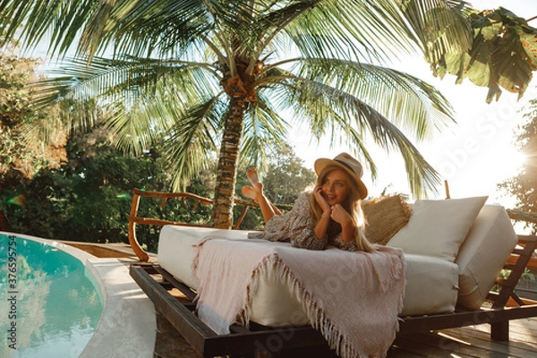 Fototapeta Enjoy vacations in luxury hotel with swimming pool. Relaxing young caucasian beautiful female resting in vacation on summer season with hat at resort swimming pool edge with chair beach on side