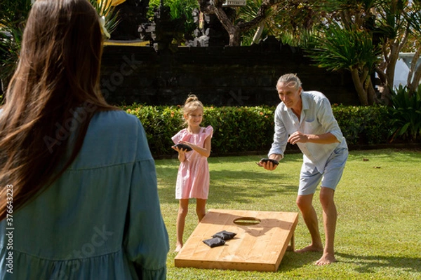 Fototapeta Happy family playing cornhole game outdoor on sunny summer day. Parents and children playing bean bag toss