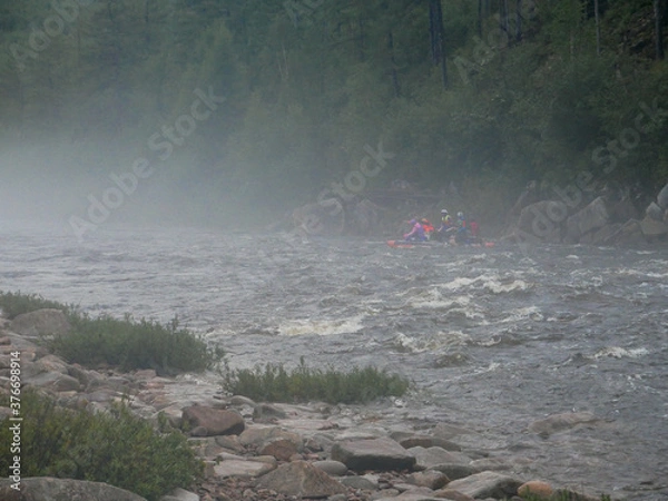 Obraz big waves on a mountain river rocks and a swimming vehicle with people on the background of mountains and forests in the fog