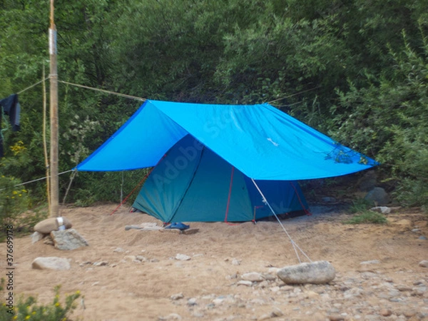 Obraz green tourist tent under a blue awning in the forest on a hike