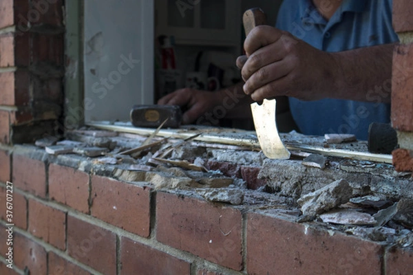 Fototapeta Workman removing excess mortar from a window opening in a brick wall during renovations