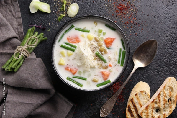 Fototapeta Creamy soup with salmon, asparagus beans, potatoes and croutons in a deep bowl on a black background. Flatlay, horizontal. Background image, copy space
