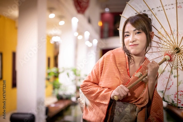 Obraz A beautiful Asian woman in traditional Japanese kimono  with an umbrella,  looking at the camera. Japanese concept of kimono and yukata.