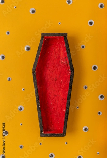 Fototapeta Halloween yellow background with an open red-black coffin in the center, around a scattering of plastic eyes of different sizes. A place for your product.