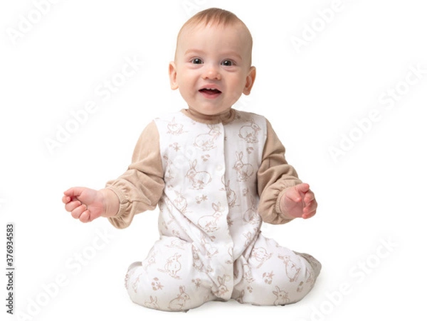 Fototapeta The baby in light clothes sits on his knees on a white background. Smiling happily looking at the camera.
