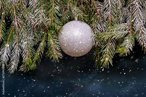 Fototapeta Silver Christmas ball on a snowy Christmas tree during a snowfall