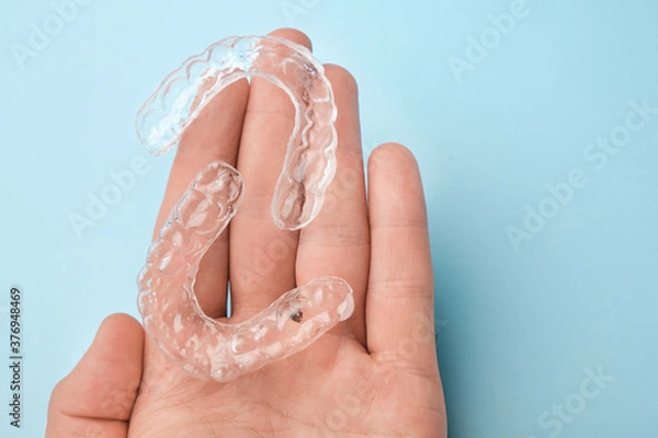 Obraz Close up mans hand holding invisible aligners for whitening and straightening of teeth on the blue background. Orthodontic therapy after brackets. Teeth healthcare