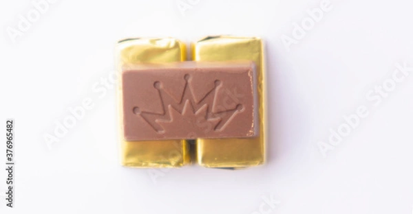 Fototapeta .Chocolate wrapped in gold paper, close-up of a few ounces of chocolate. On a white background