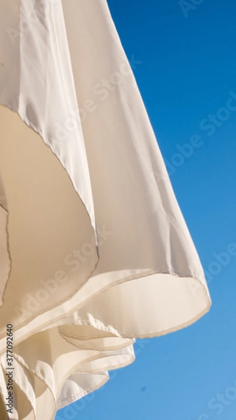 Obraz White parasol, blue sky background, wind movement, shadows on white textile