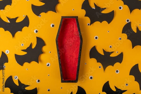 Fototapeta A Halloween yellow background with many plastic eyes, bats and an open black and red coffin in the center. Festive flat lay. A place for your product.
