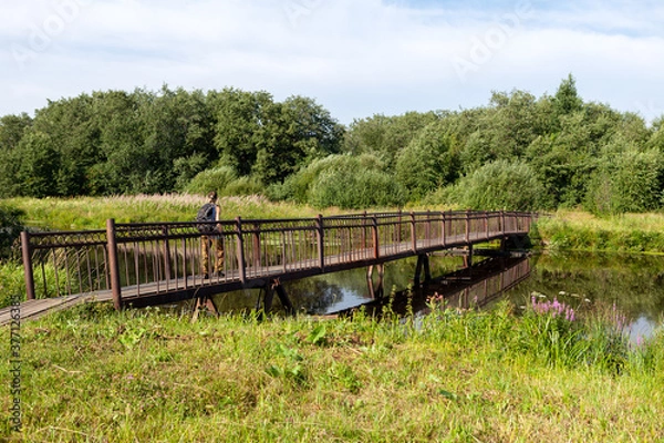 Fototapeta A tourist walks on a pedestrian wooden bridge over the river