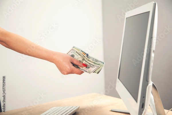 Fototapeta Close-up of hands shopping paying online using laptop while holding US dollars