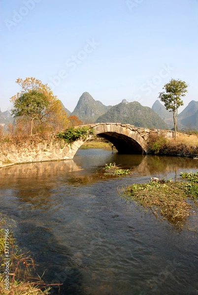 Obraz Scenery along the Yulong River near Yangshuo, Guilin in Guangxi Province, China. An ancient stone bridge near Yangshuo. The old bridge crosses a stream connecting farmland near to the Yulong River.